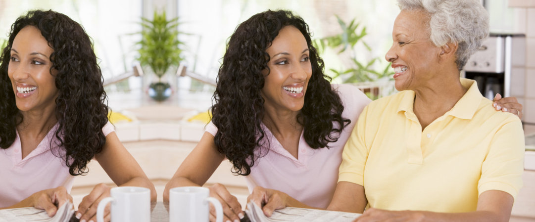 Close up of two women in kitchen with newspaper smiling