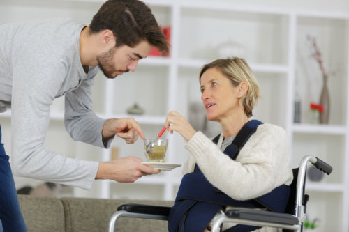 Caregiver giving cup of tea to disabled women in wheelchair