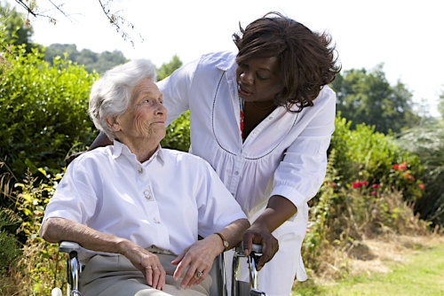 afro-american caregiver talking to disabled senior women outdoors